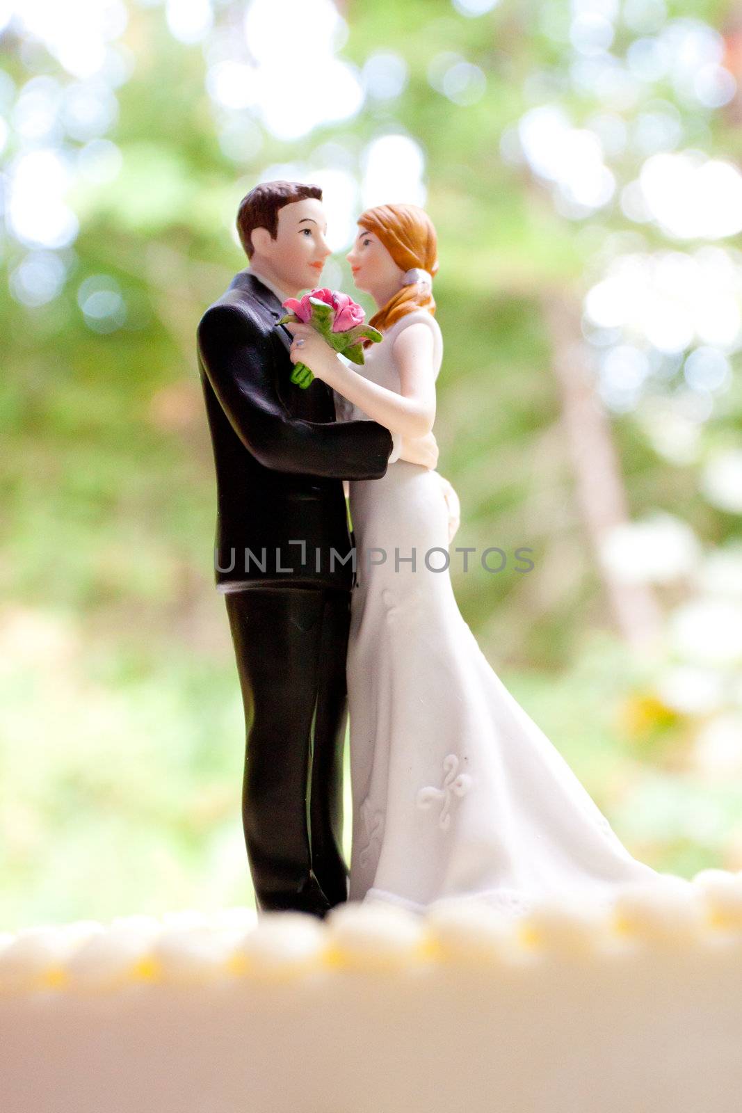 A bride and groom cake toppers stands atop this traditional white wedding cake at a reception in the woods or forest.