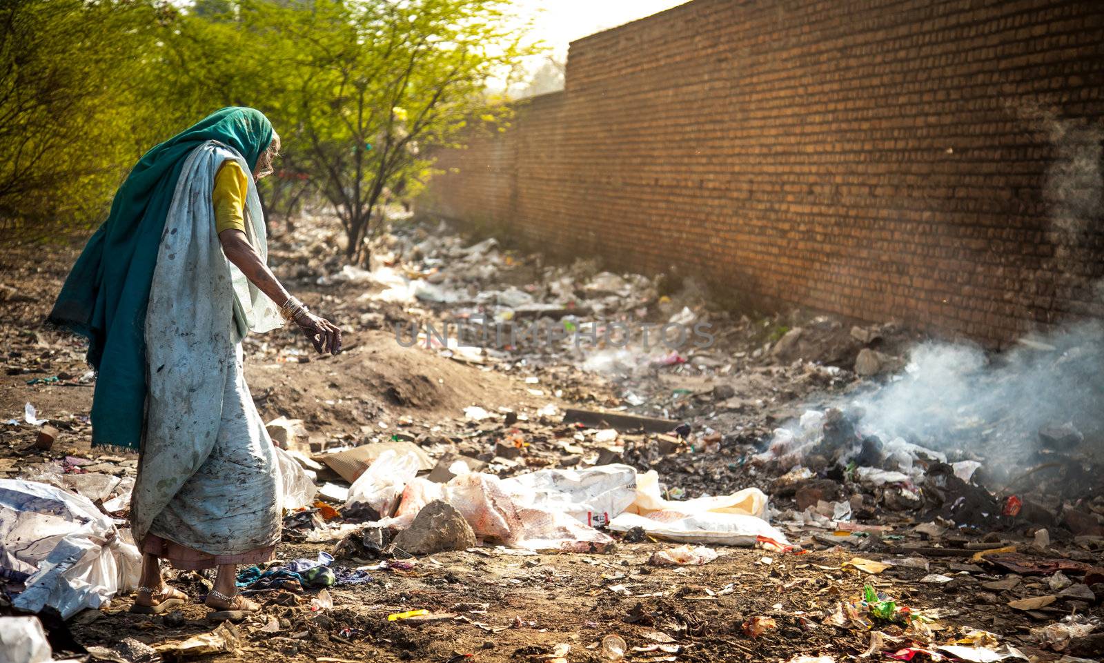 Pollution and poverty : Indian old female sitting  for warmup  herself near fire  in  garbage,