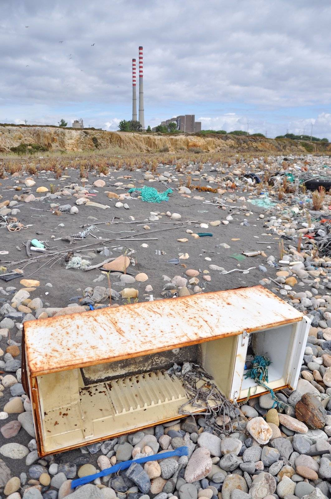 Trashed fridge on the seashore next to a factory by anderm