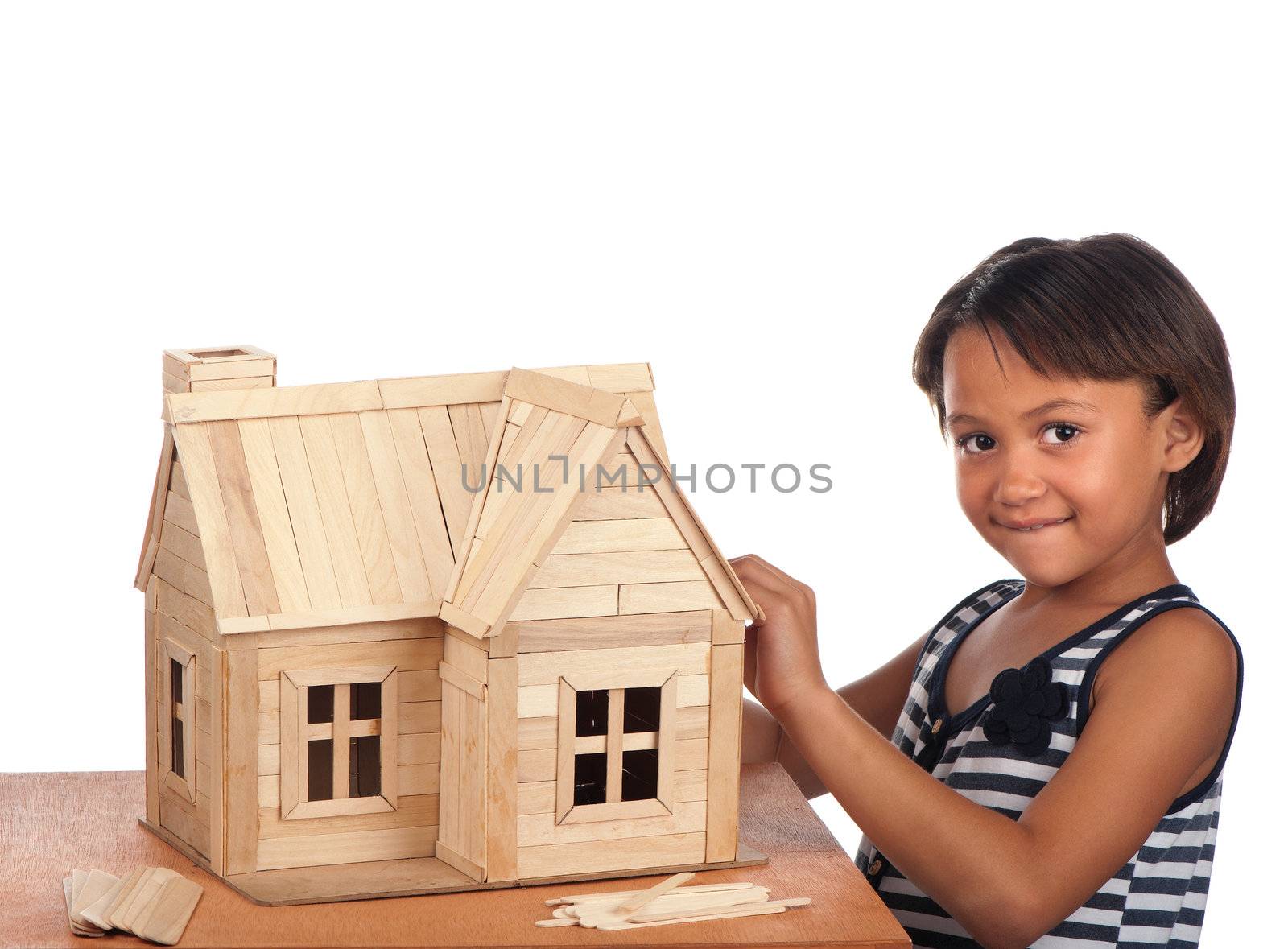 A smiling young girl stands next to the popsicle house she is building.