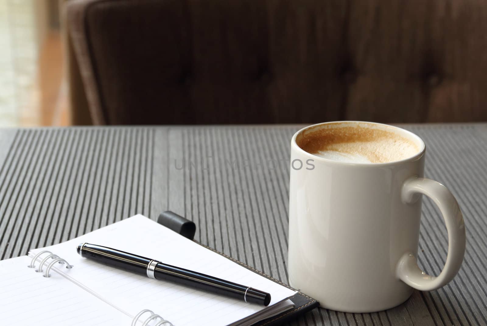 Hot coffee latte in white cup with journal book and pen
