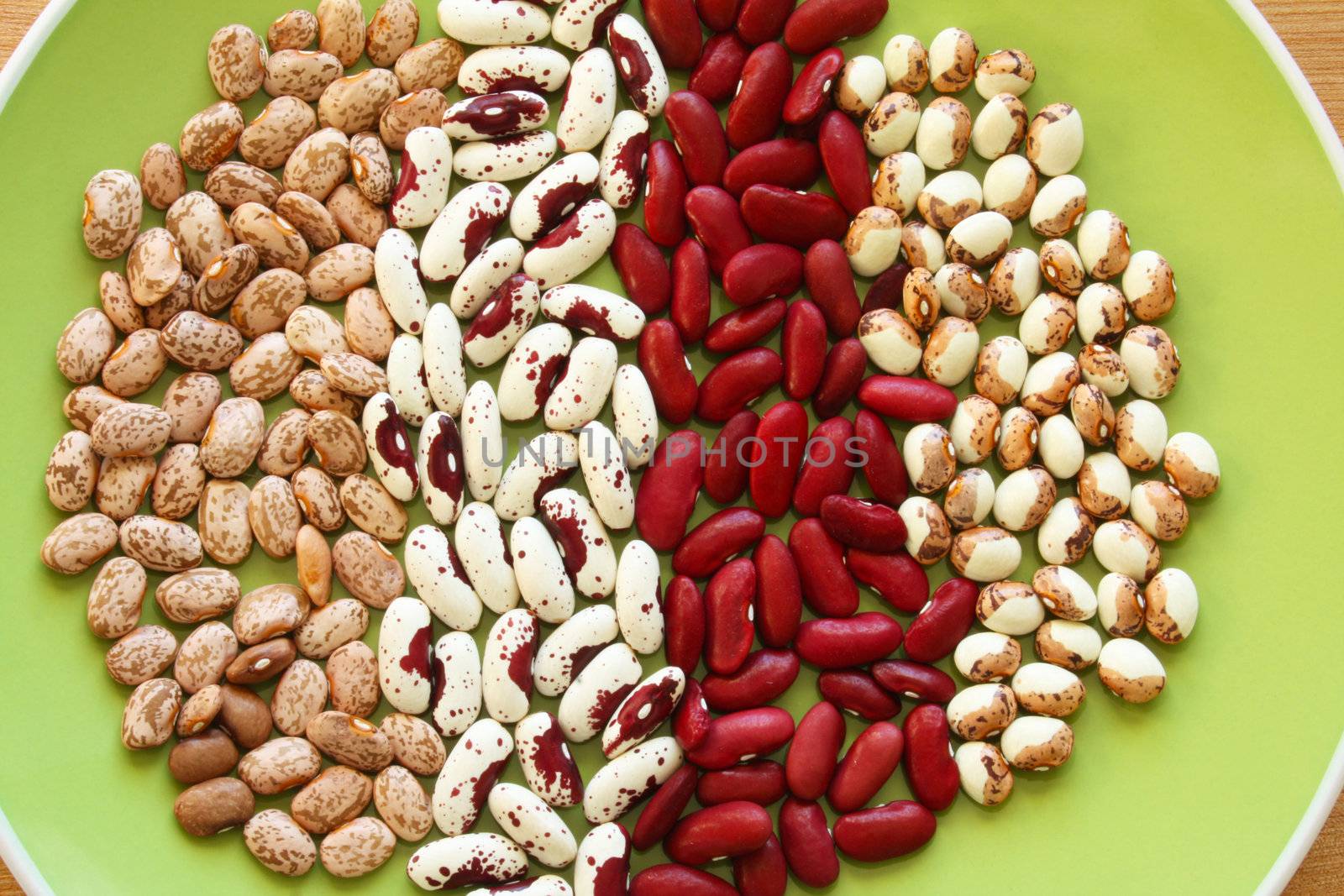 A background or wallpaper image of four varieties of heirloom soup bean in strips on a green plate.