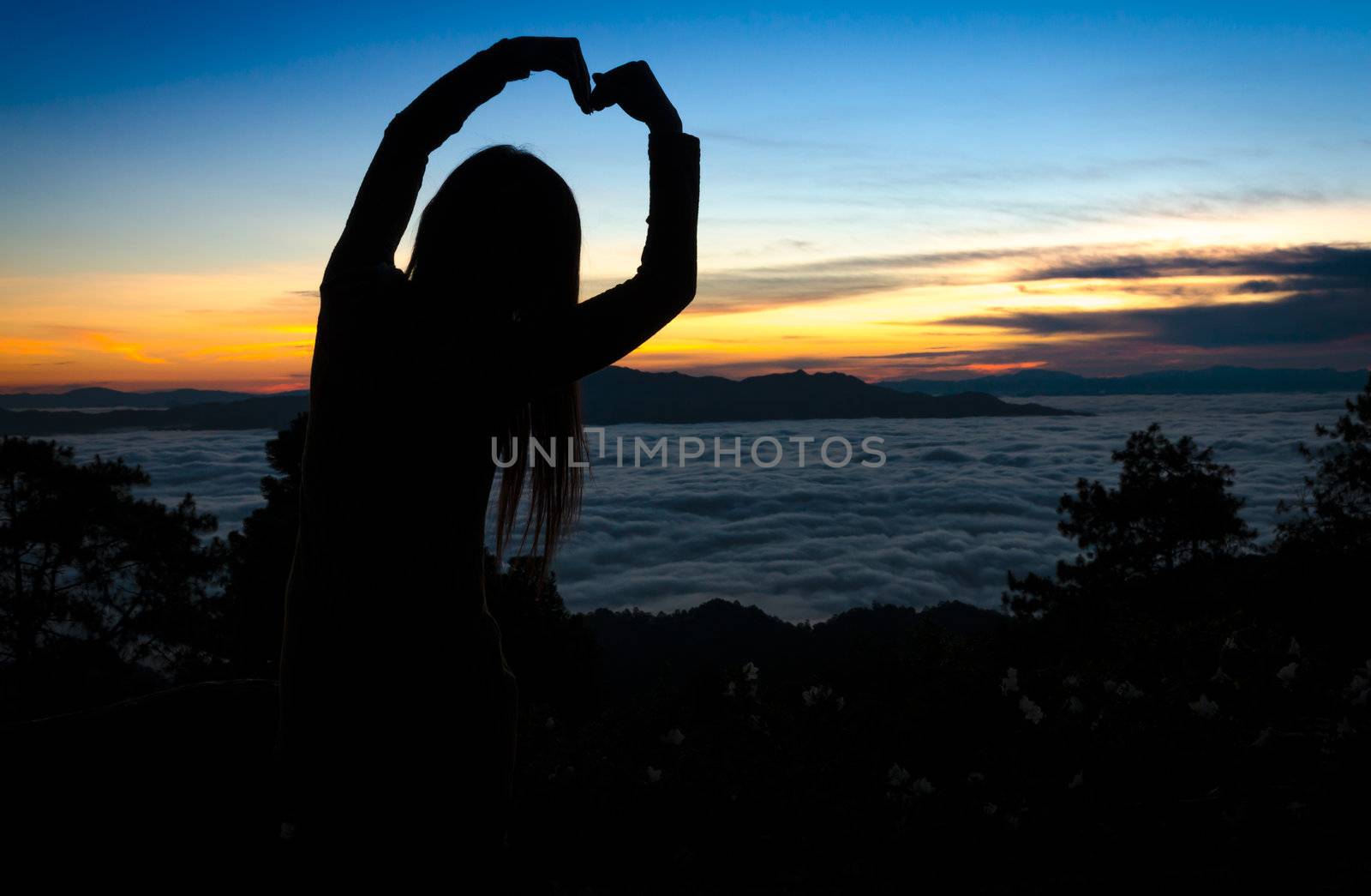 Silhouette of woman making heart shape with arms over sunset