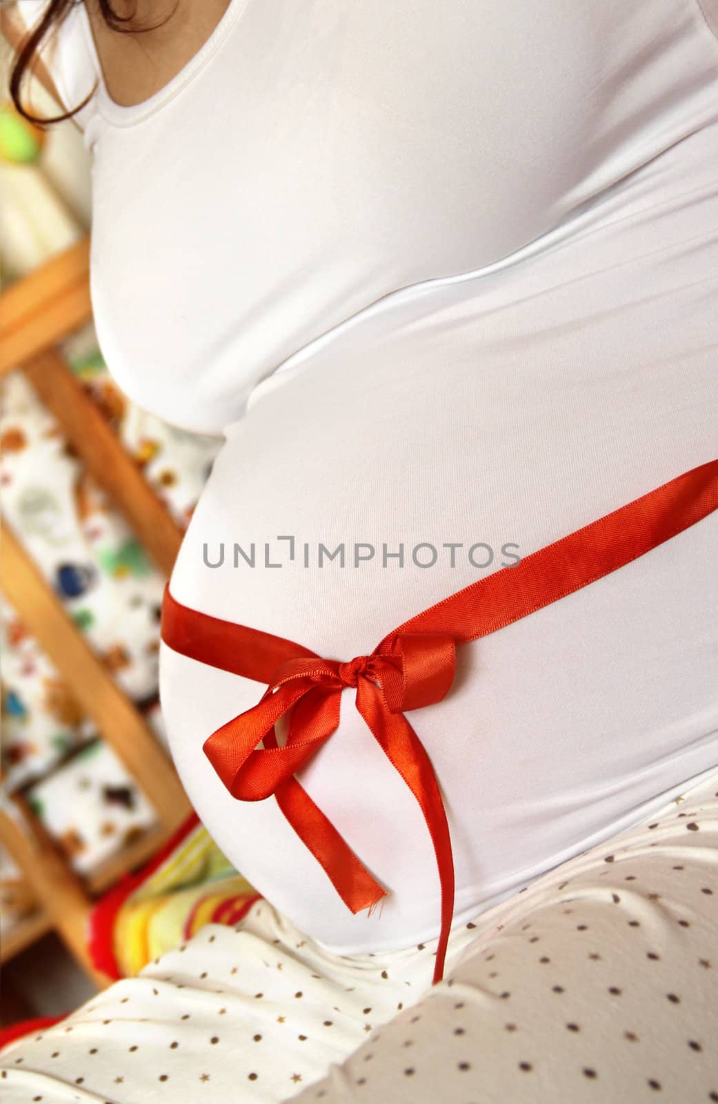 Pregnant woman tummy decorated with red ribbon and bow 