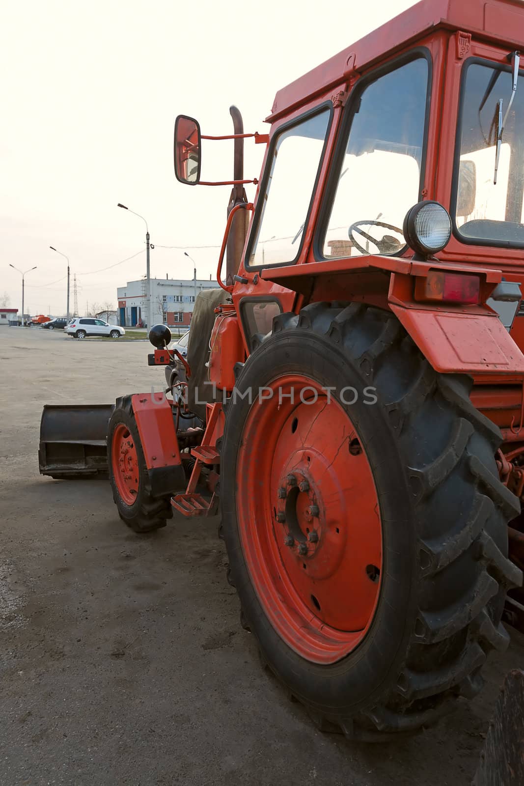 Red wheel tractor with  shovel in  parking lot on sky background.