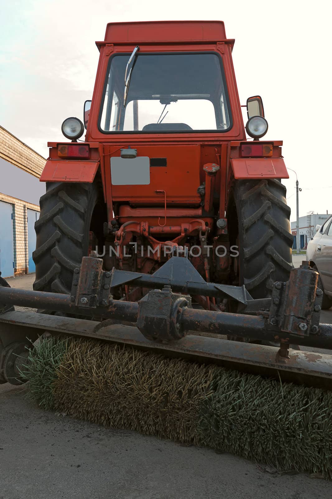 Red wheel tractor with fetlock in  parking lot on sky background.