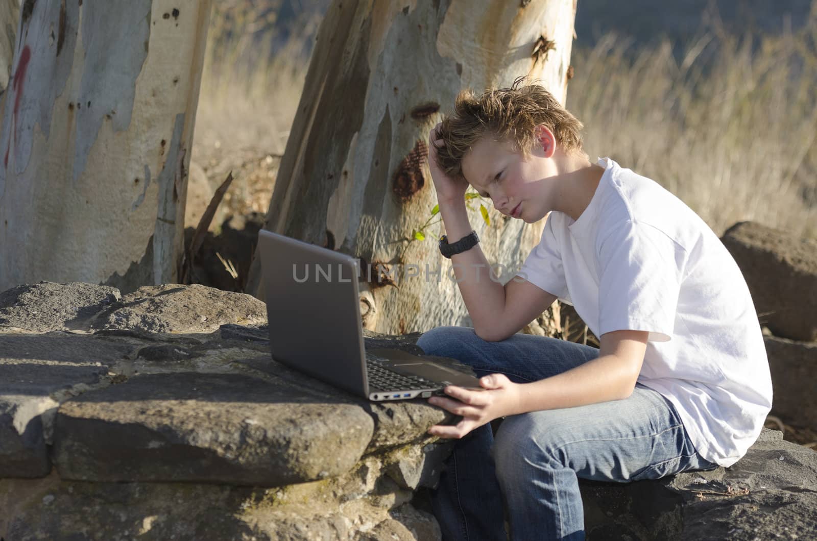 Thoughtful teenager sits on nature with laptop