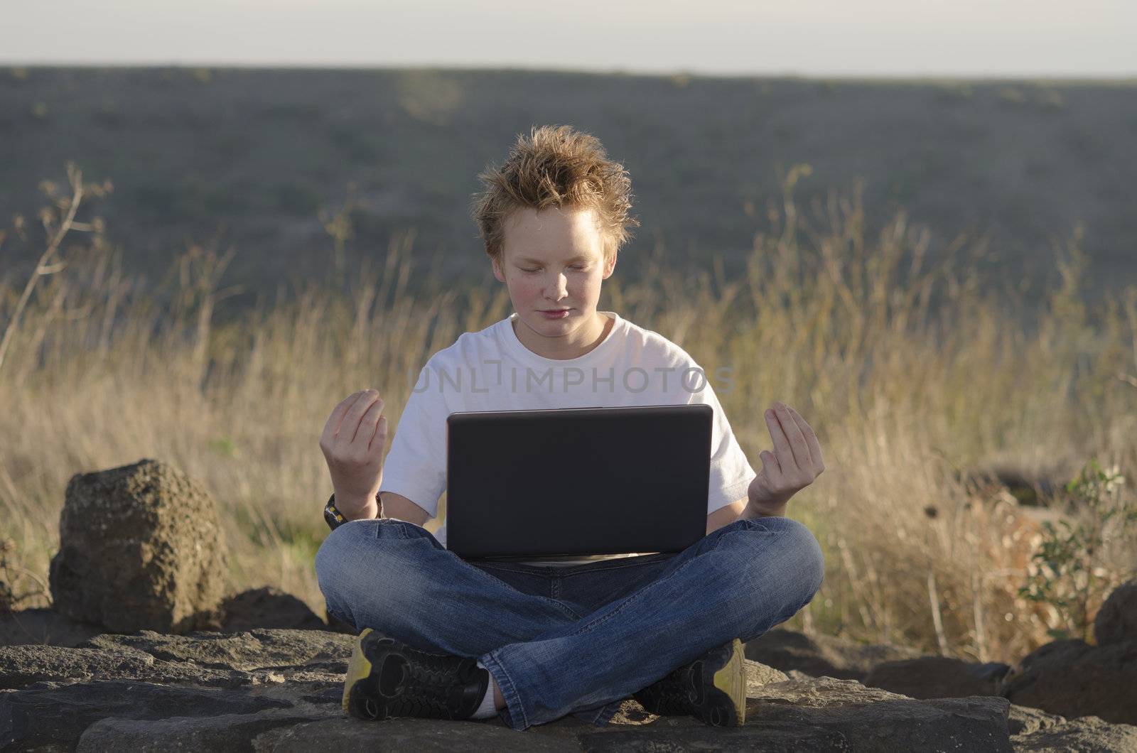 Pretty guy with laptop meditating in nature at sunset