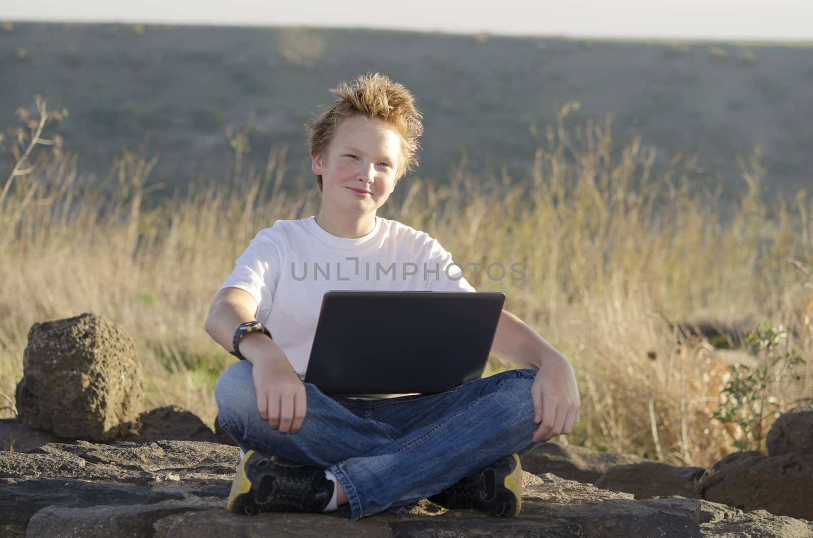 Attractive teenager with mobile computer sits on the stone at sunset