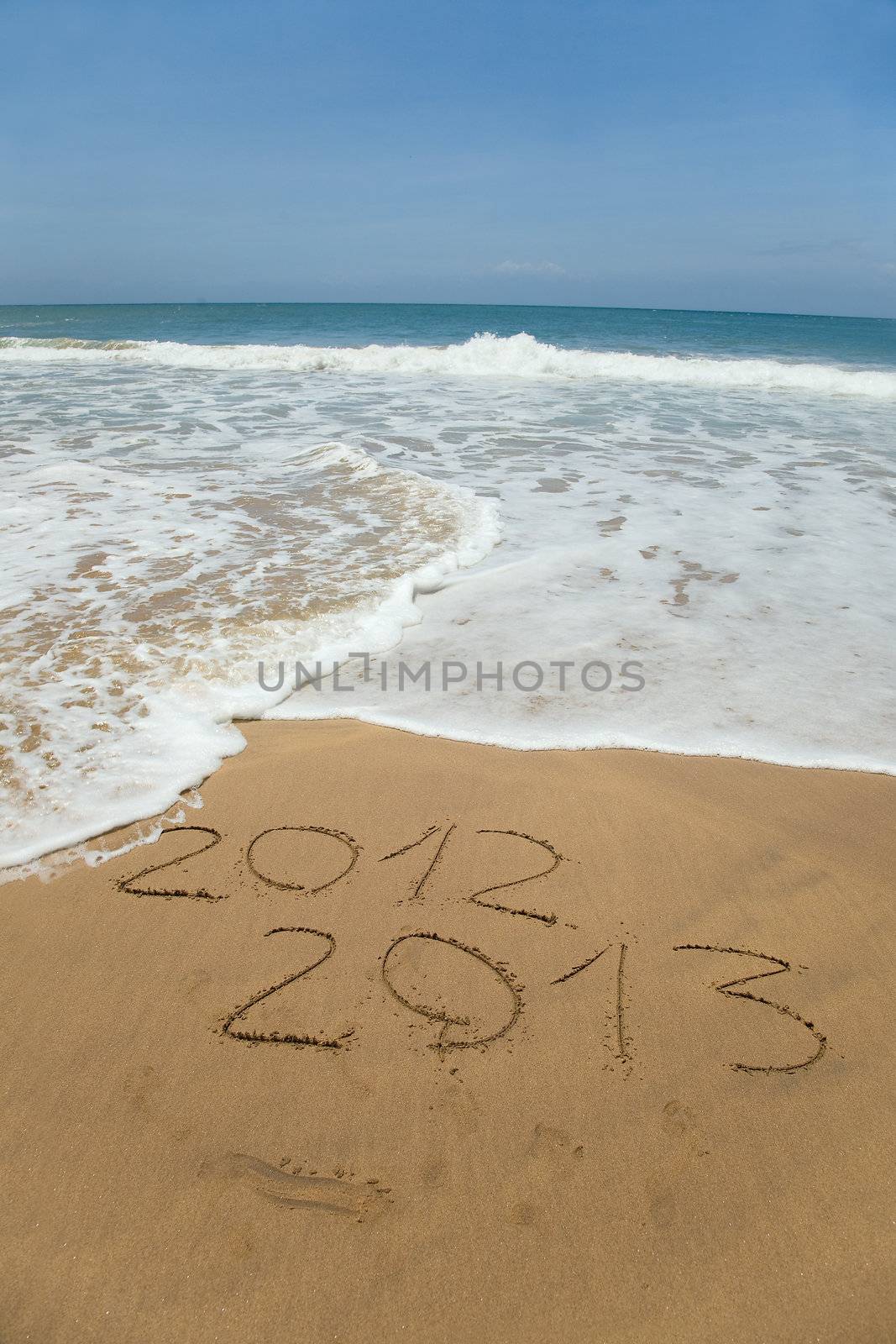 2012 and 2013 written in sand on beach with sea waves starting to erase the word 