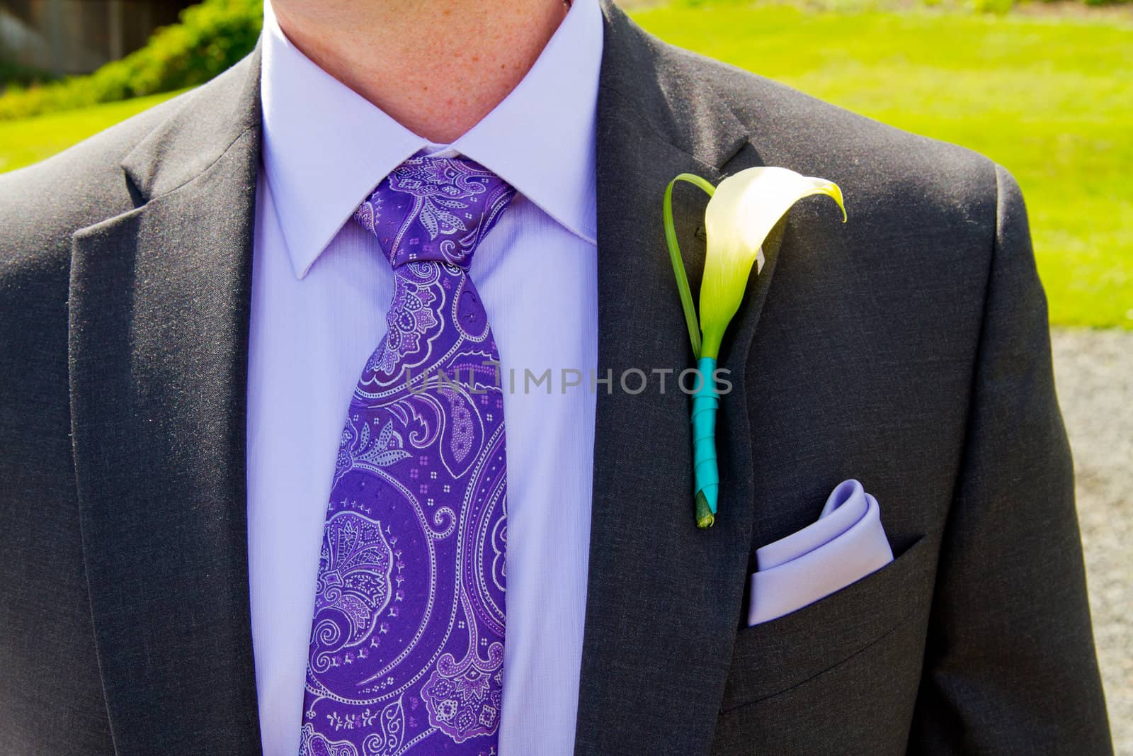 A groom and his boutonniere on his wedding day. He is wearing a suit with a single flower on the lapel of his jacket.
