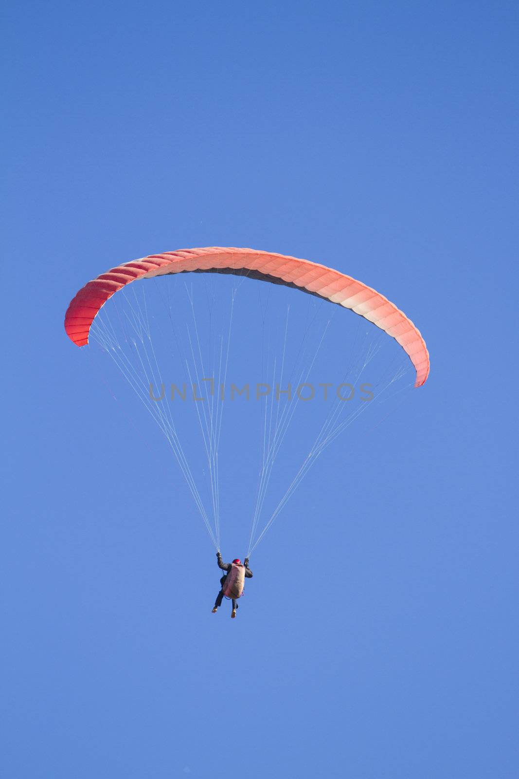 A paraglider takes to the sky. Shot from below against a blue sky.