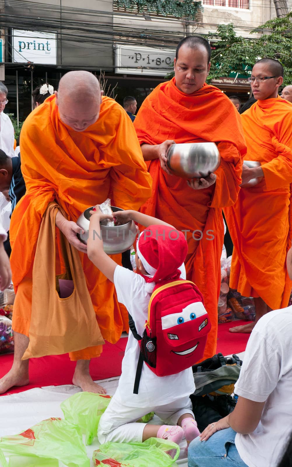 BANGKOK - DECEMBER 23: Boy with a Santa Claus hat giving alms at a mass alms giving in the morning at Soi Thonglor in celebration of the 2,600th anniversary of Lord Buddha's enlightenment on December 23, 2012 in Bangkok, Thailand.