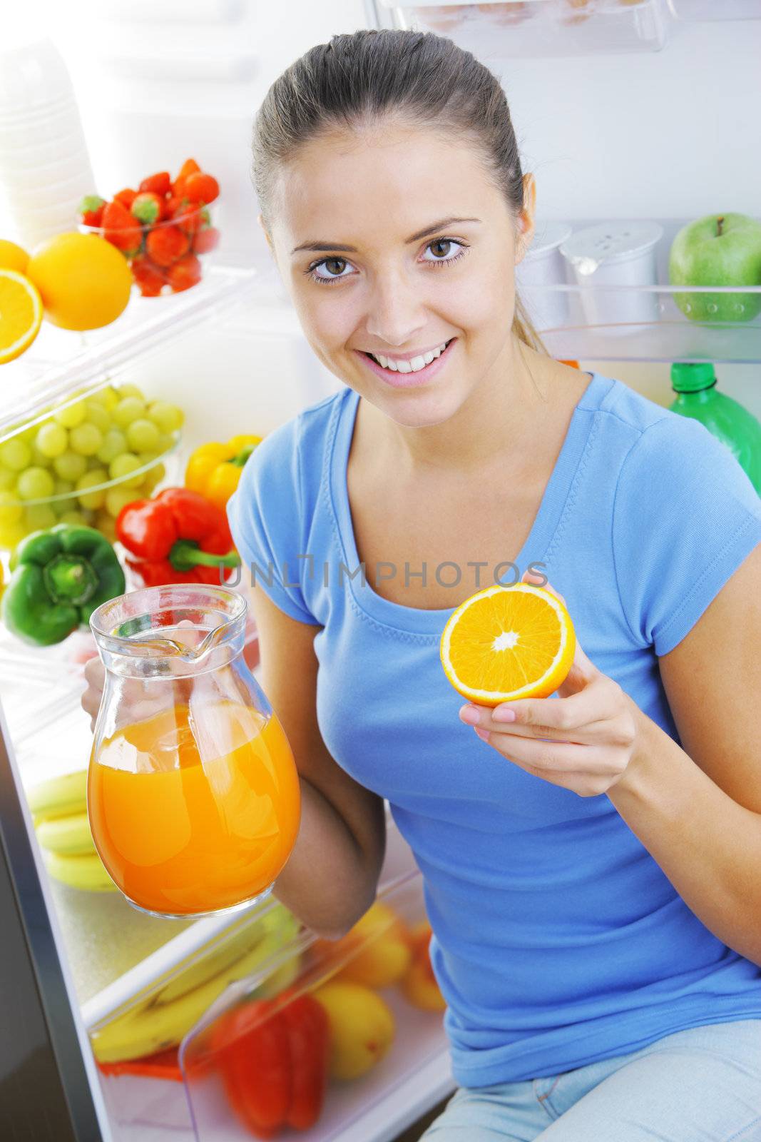 Beautiful young woman near refrigerator with a carafe of orange juice