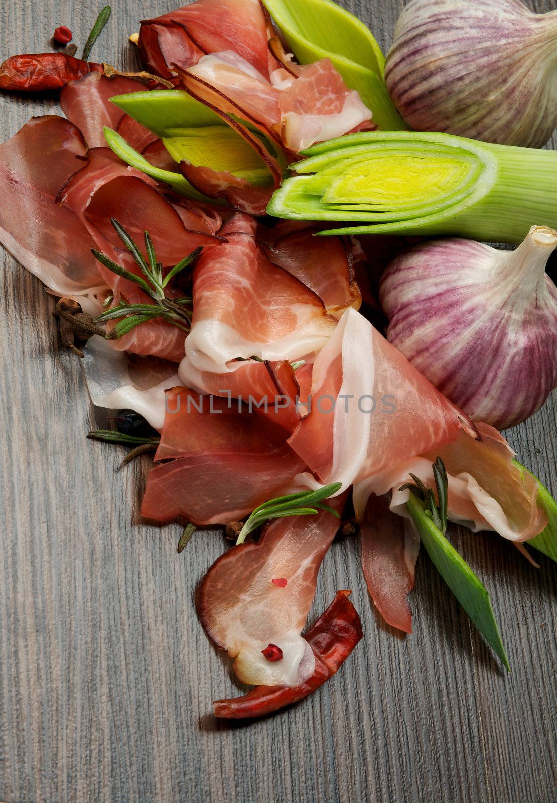 Slices of Perfect Jabugo Ham with Ripe Leek and Garlic closeup on Dark Wood background