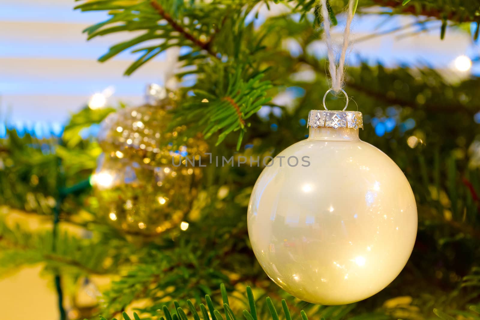 Elegant beautiful Christmas tree ornaments hang from this fir with lights and decorations all around.