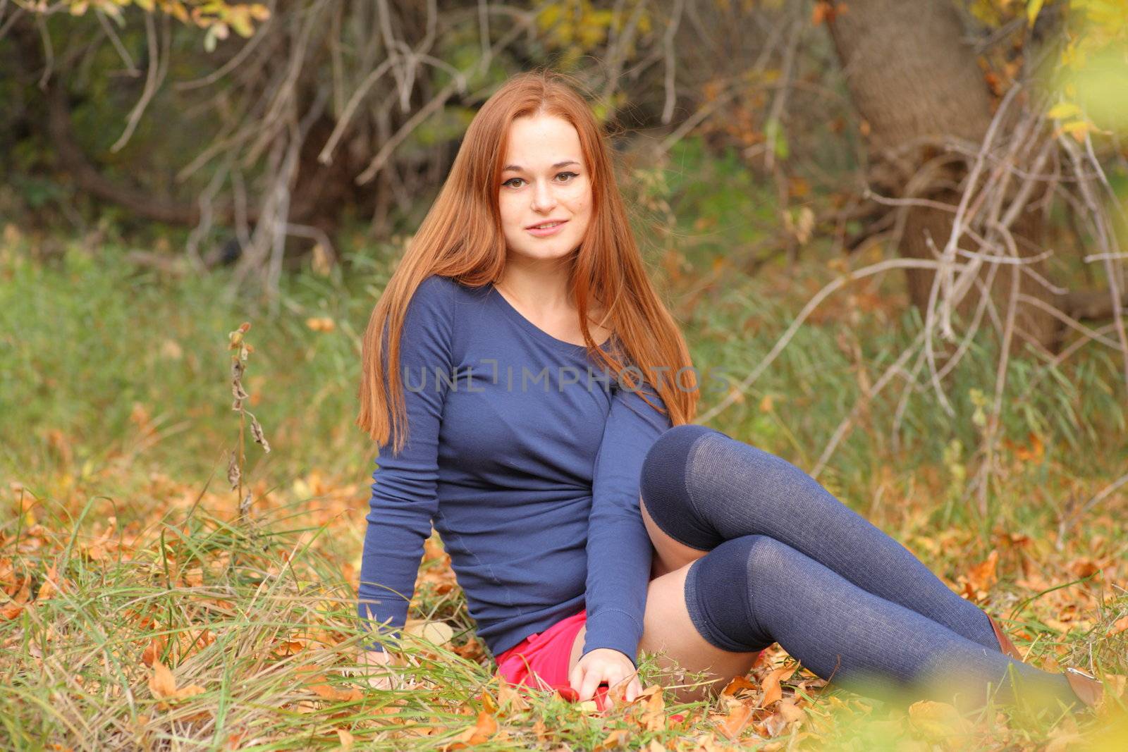 romantic redhead girl sitting in autumn leaves