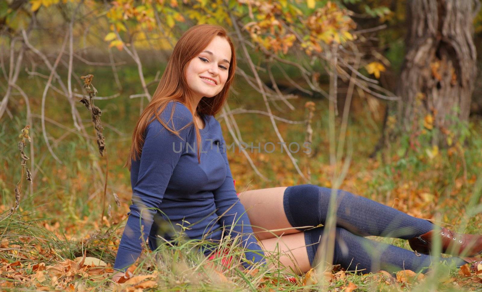 romantic redhead girl sitting in autumn leaves