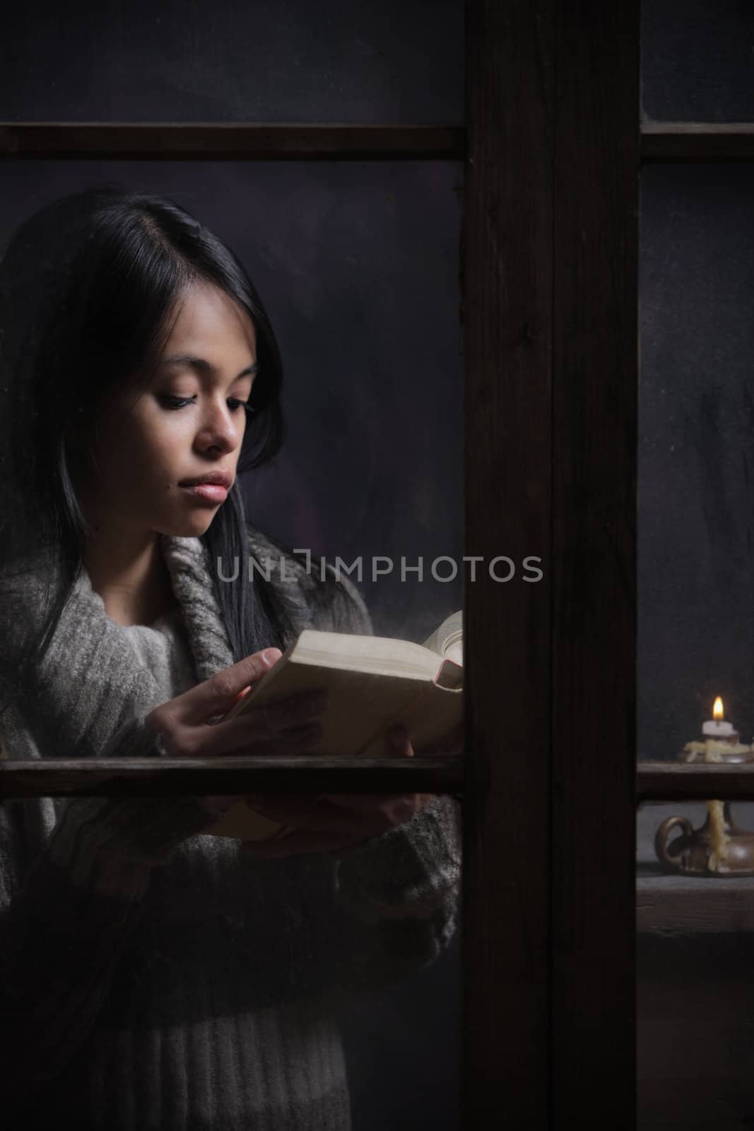 Portrait of a beautiful woman behind window reading a book 