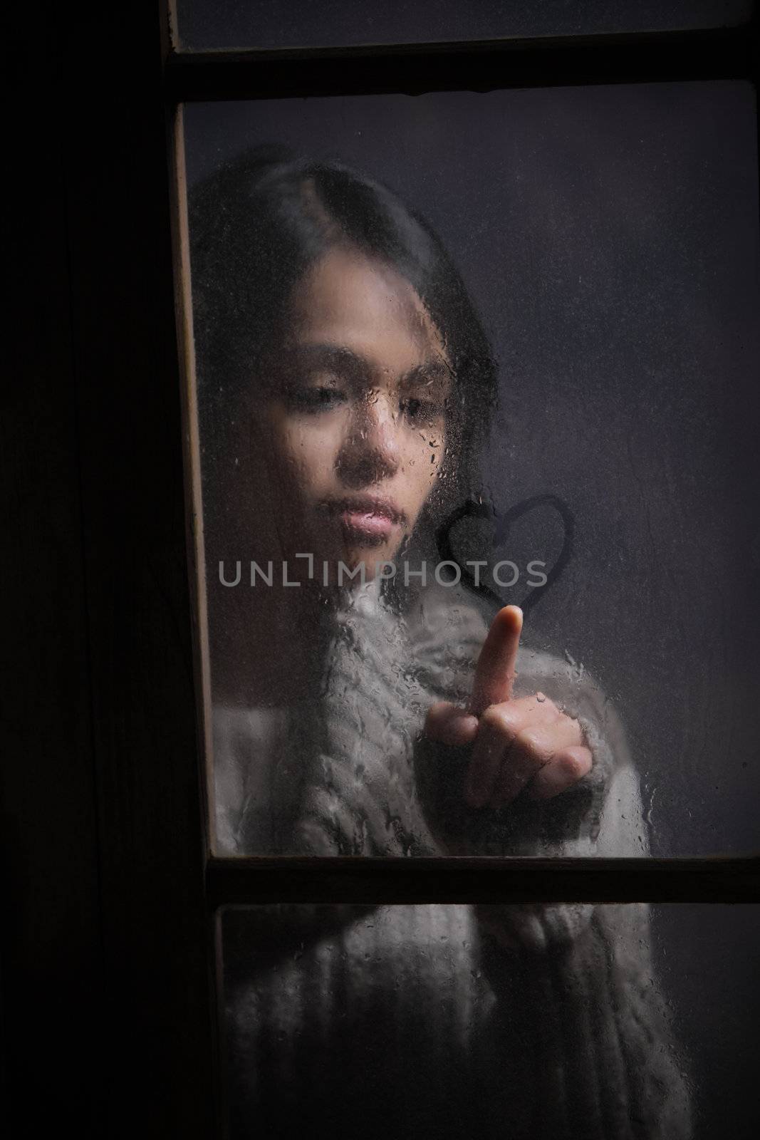 Portrait of woman drawing heart on wet window, focus on rain drop
