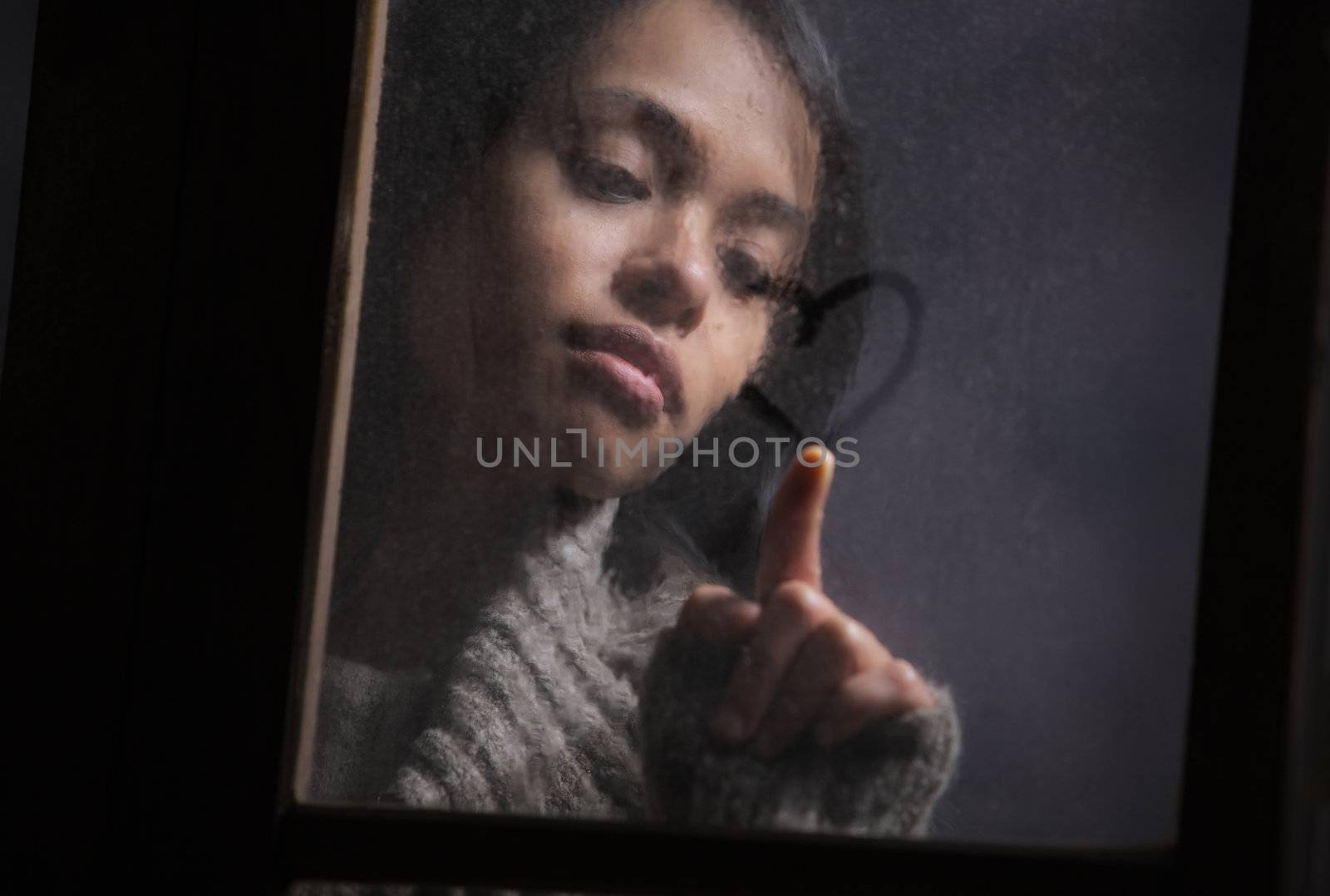 Portrait of woman drawing heart on wet window