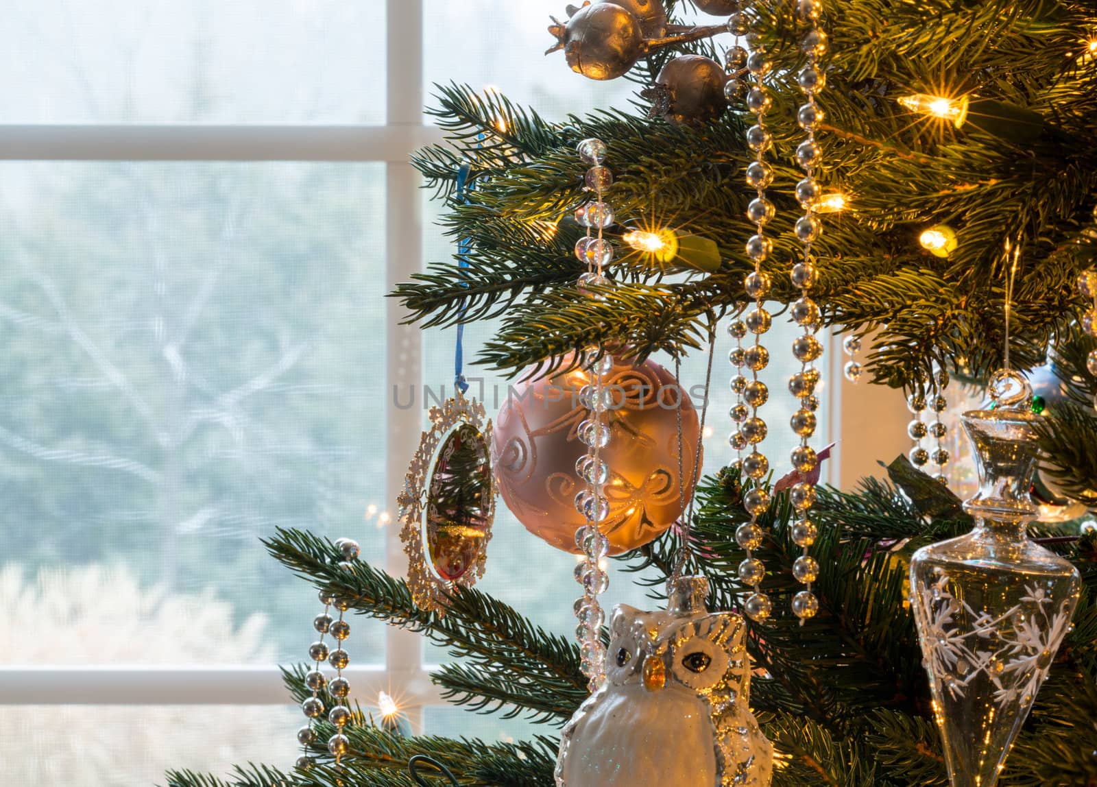 Macro shot of christmas tree decorations on indoor tree as snow falls outside window