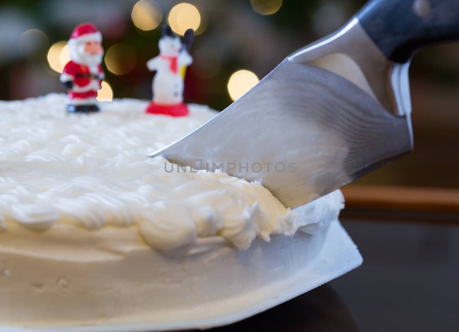 Slice out of iced christmas cake with lights of xmas tree out of focus in background