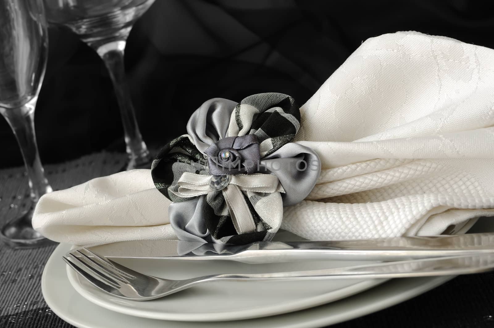 Decorative folded napkin with a clamp in the shape of a flower on a plate with cutlery