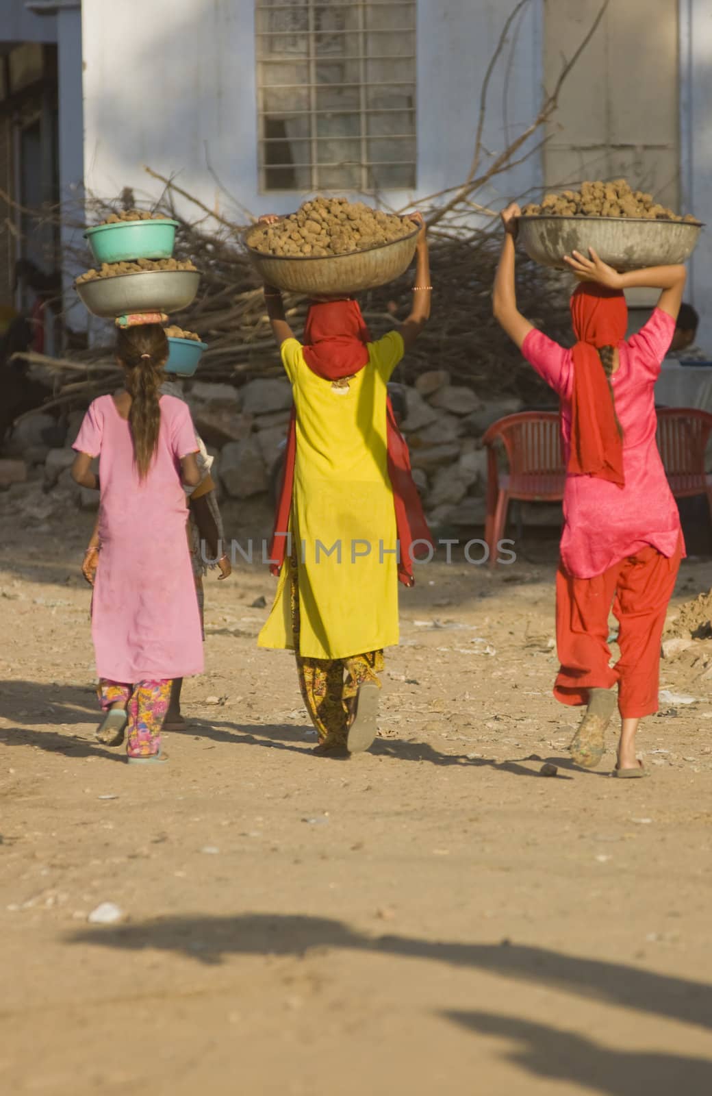 Indian teens carrying baskets containing camel dung for use as fuel at the Pushkar fair Rajasthan India