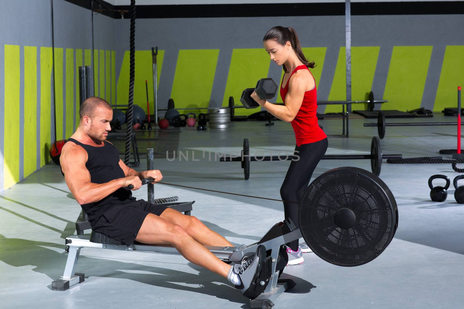 Gym couple with dumbbell weights and fitness rower by lunamarina