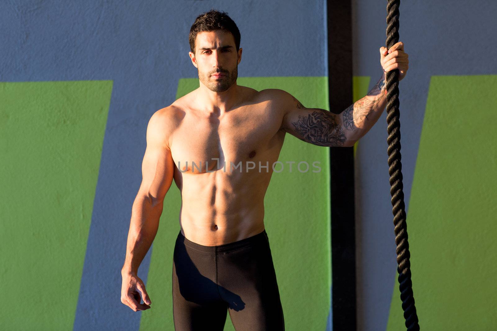 Crossfit gym handsome man holding hand a climbing rope