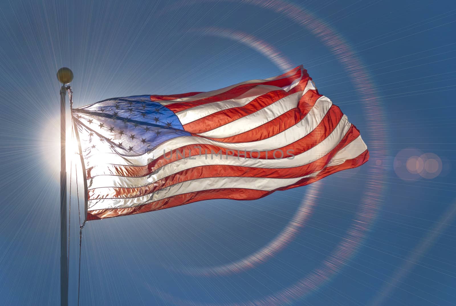American flag, back lit by the sun, waving in the wind with lens flare