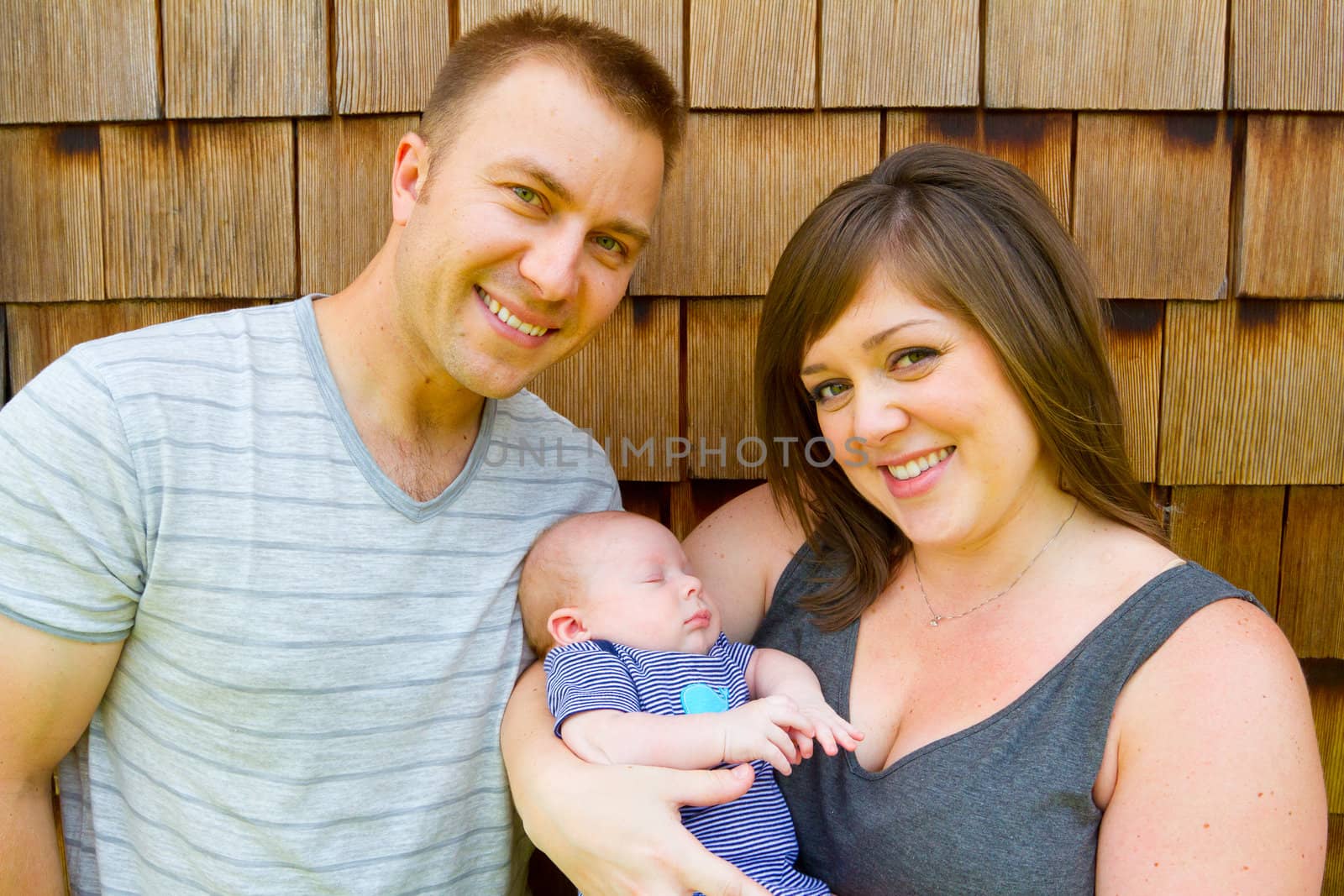 An attractive couple holds their newborn baby in their arms.