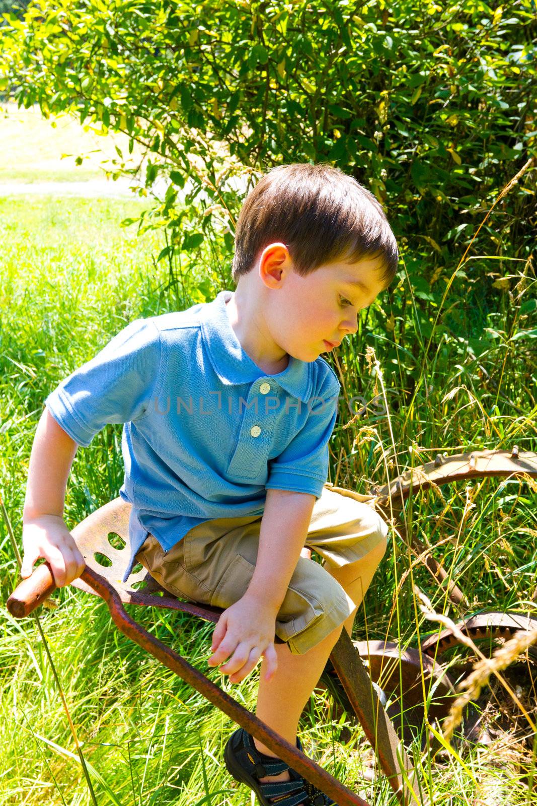 A young child is playing in a blue polo shirt near some farm equipment outdoors.