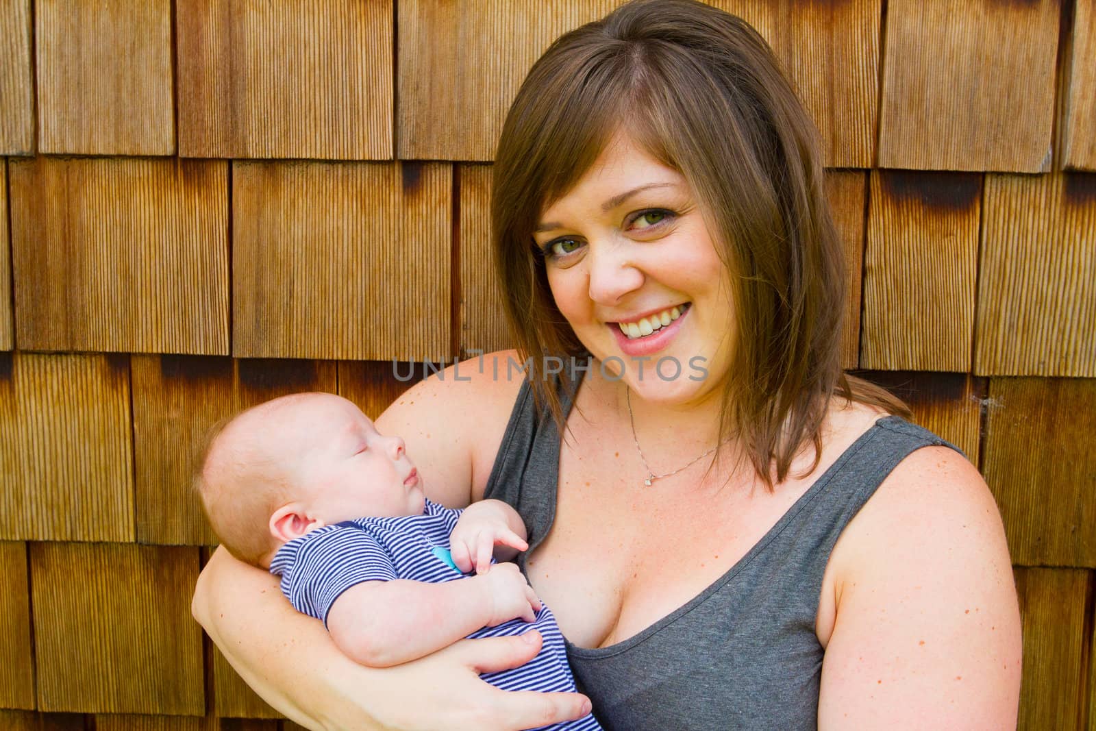An attractive woman holds her newborn baby boy in her arms outdoors.