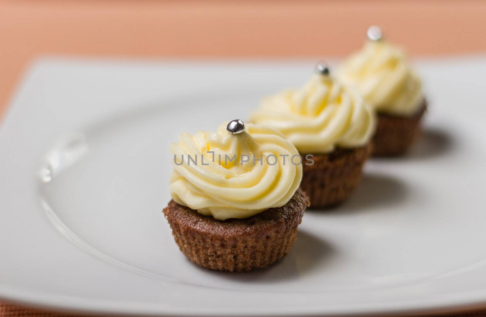 Three chocolate cupcakes with silver sprinkles on top, on white plate and fabric tablecloth