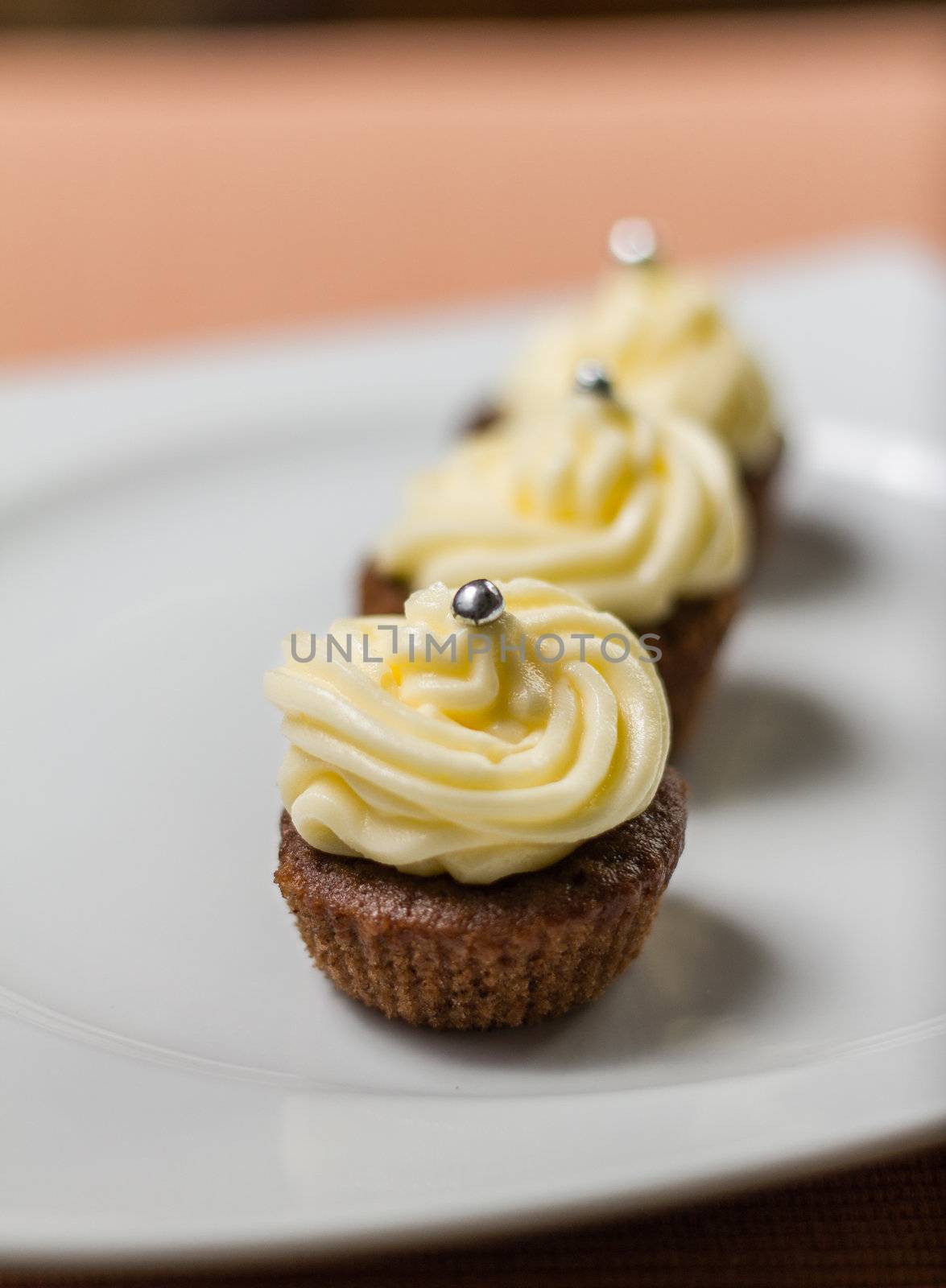 Three chocolate cupcakes with silver sprinkles on top, on white plate and fabric tablecloth