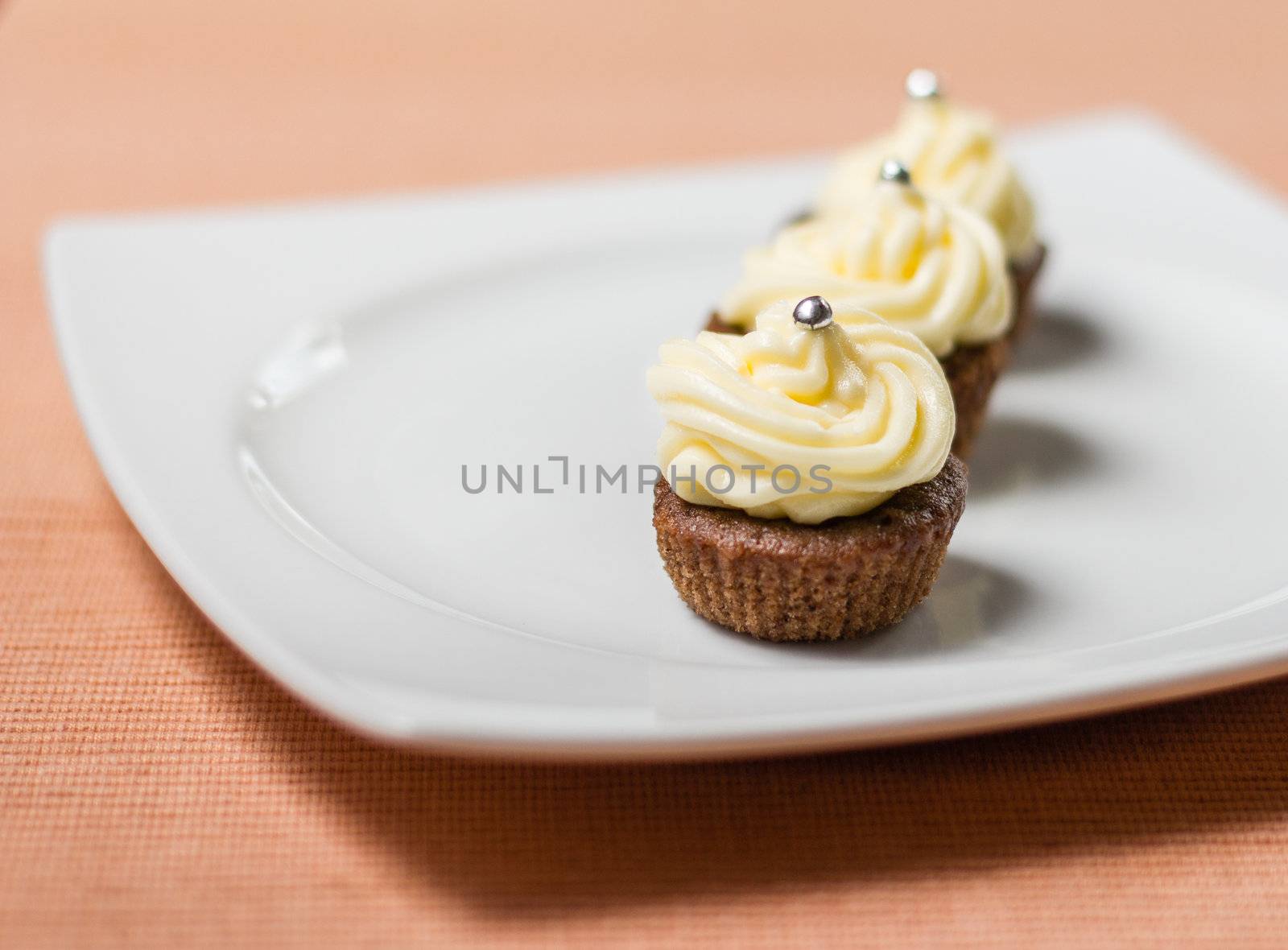 Three chocolate cupcakes with silver sprinkles on top, on white plate and fabric tablecloth