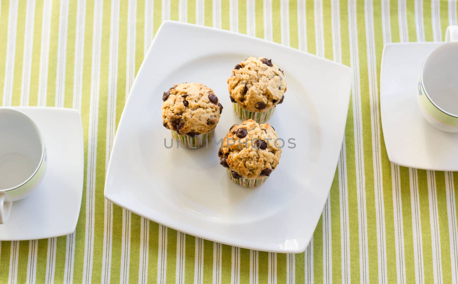 Three chocolate chip muffins on white plate and green striped tablecloth at breakfast