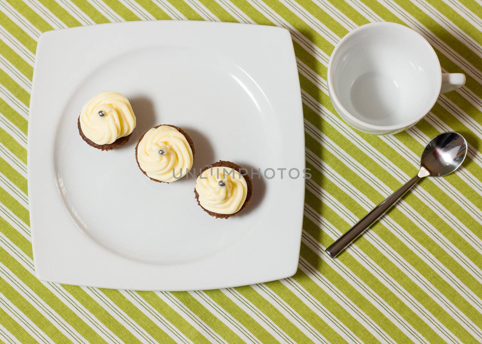 Three chocolate cupcakes with silver sprinkles on top, on white plate and fabric tablecloth with stripes