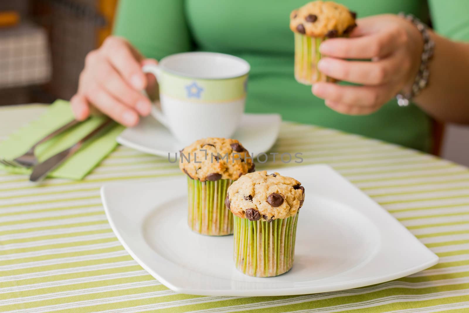 Nice girl hand taking delicious chocolate chip muffin at breakfast in green striped tablecloth