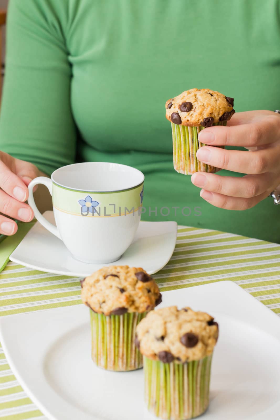 Nice girl hand taking delicious chocolate chip muffin at breakfast in green striped tablecloth