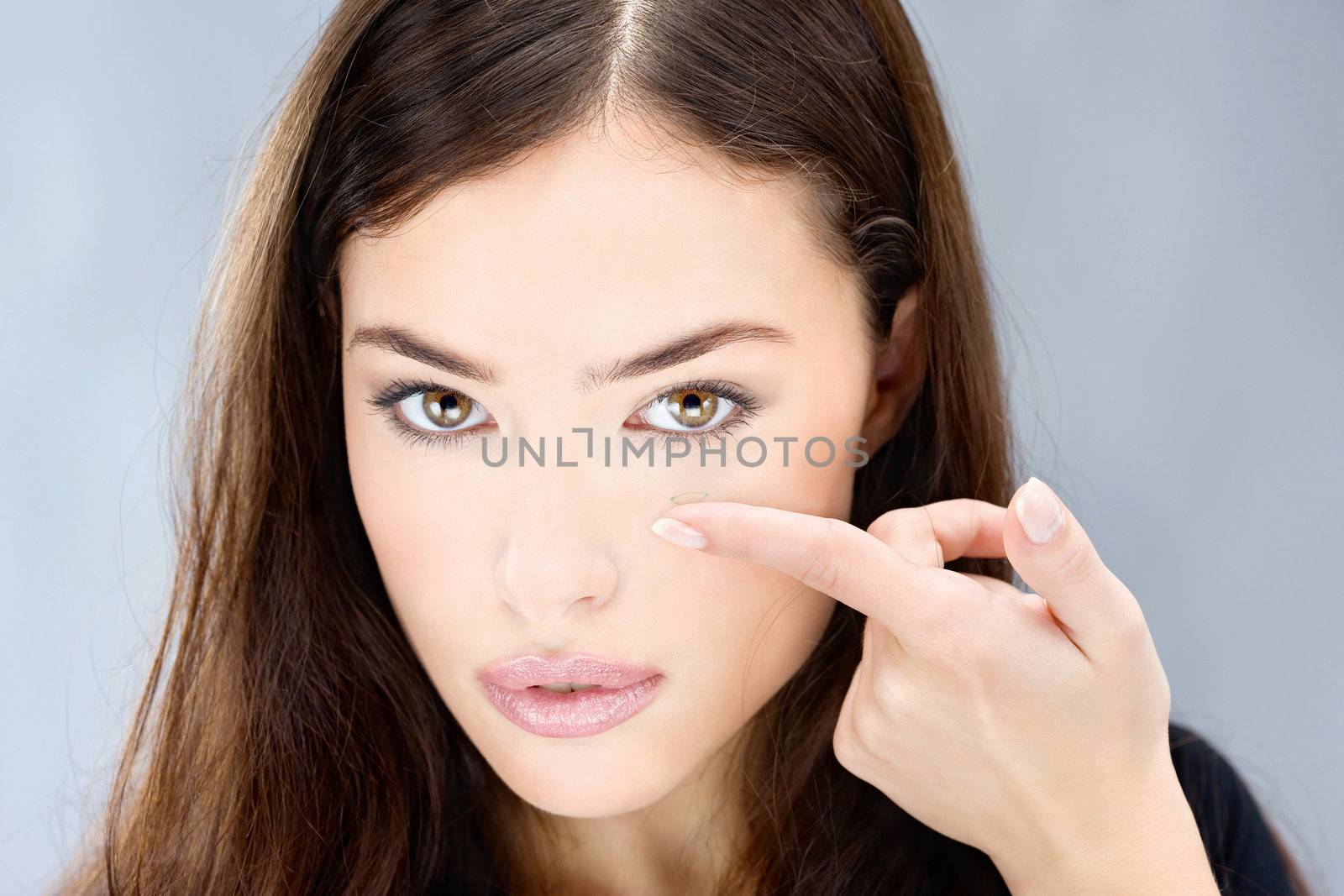 Young woman holding contact lens on finger in front of her eye