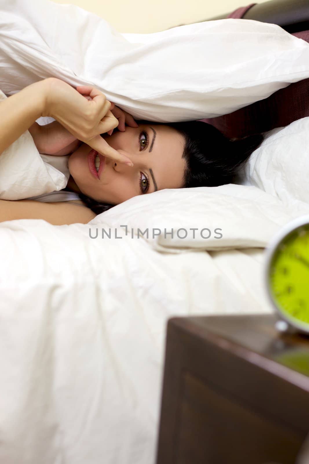 Beautiful woman hiding in bed makes silence sign under blanket by fmarsicano