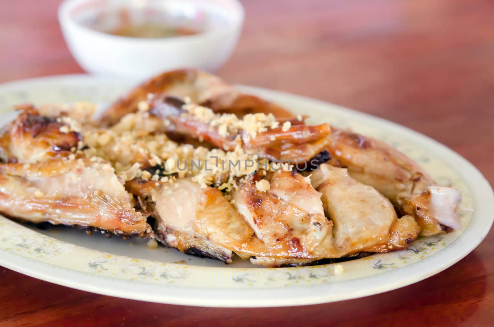 Grilled chicken with fried garlic on dish served with spicy sauce in bowl