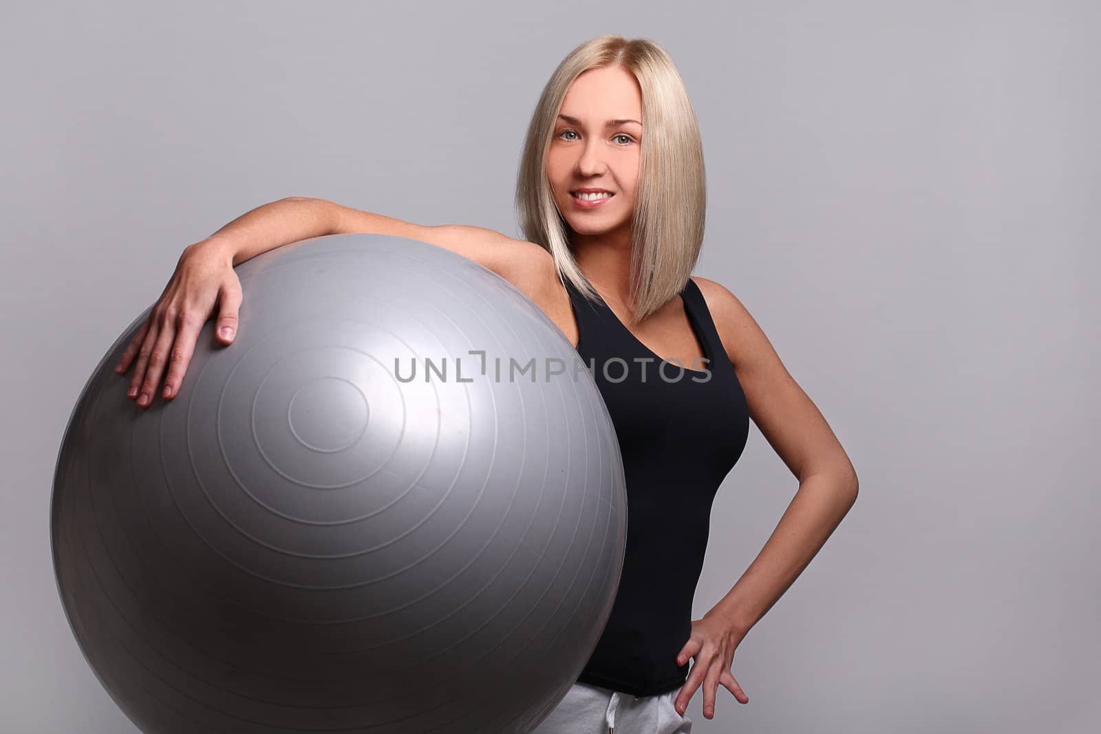 Close up of happy and beautiful woman with fitness ball isolated on a grey