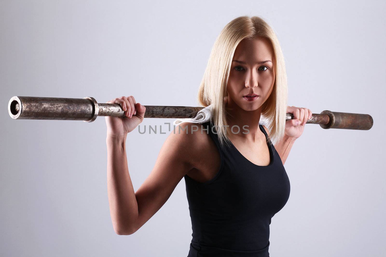 Slim and sporty young blonde doing fitness exercise with fitbar in studio