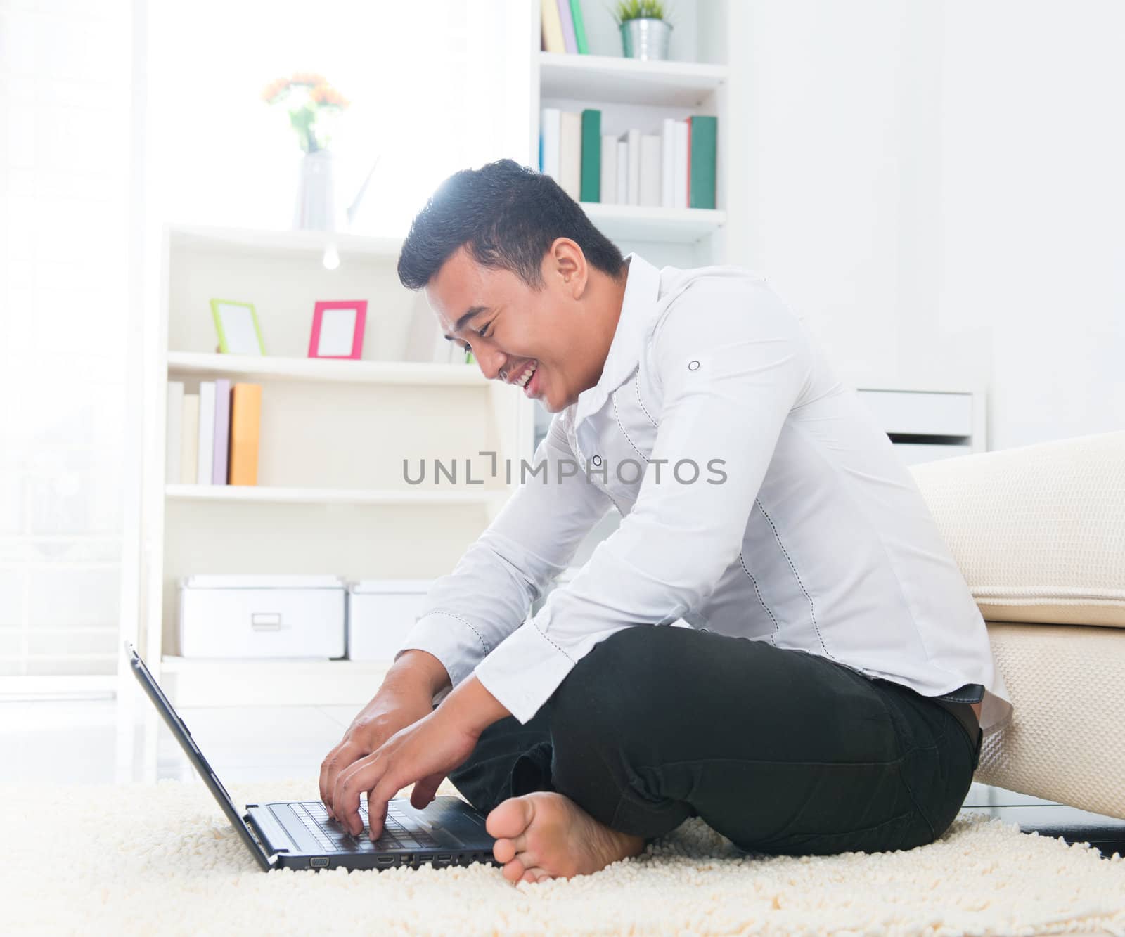 Southeast Asian man surfing internet at home, sitting on floor.