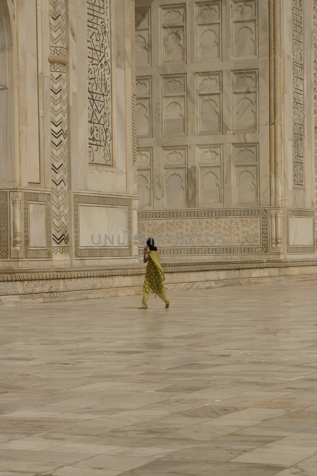 Indian woman in green sari walking past the Taj Mahal. White marble mausoleum in Agra, India.