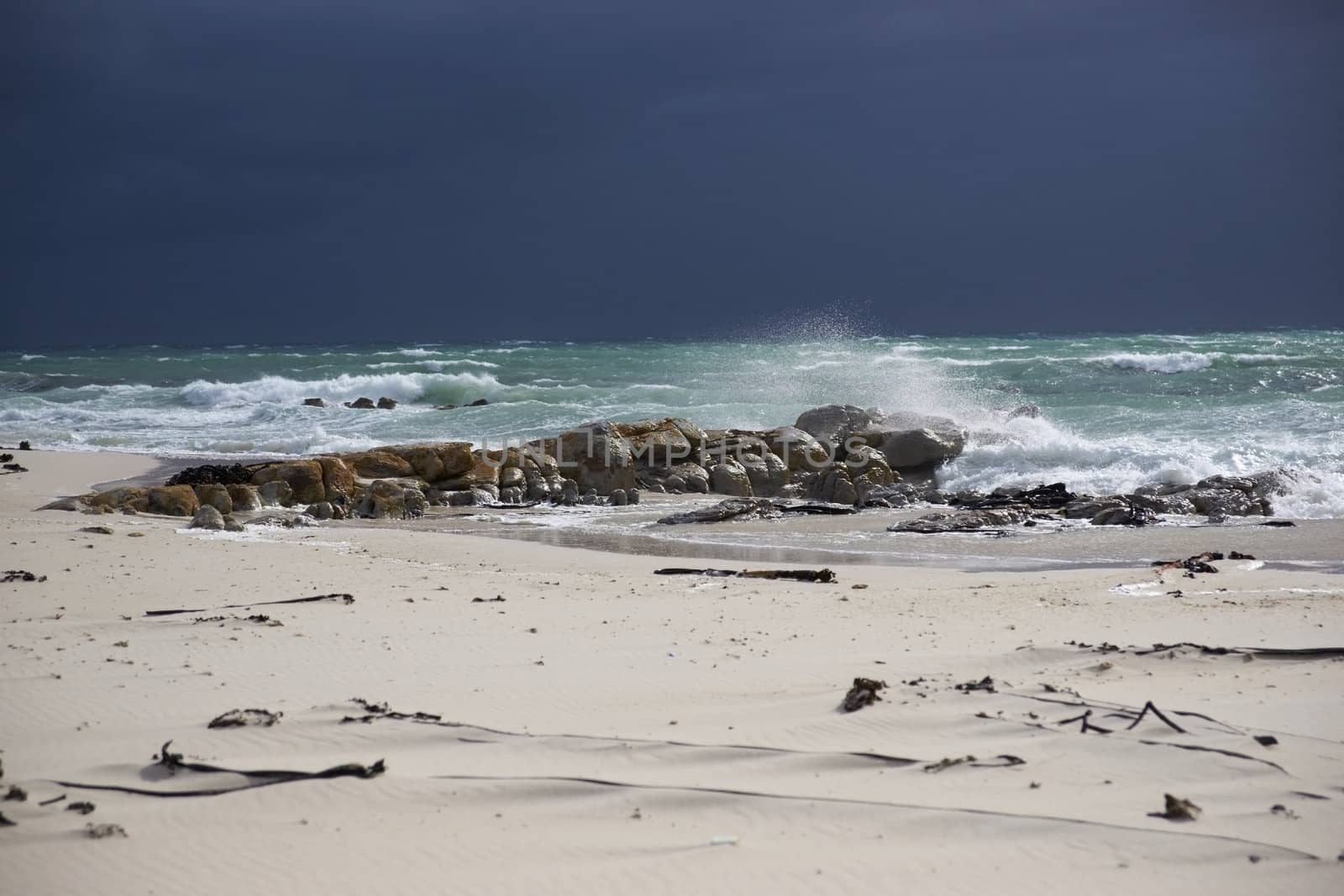 Dark clouds over a sunlit stormy sea and sandy beach on Cape Peninsula of South Africa.